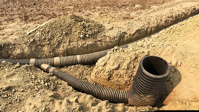 The catchment under construction — corrugated main line laid in the open trench, a branch line joining it, the riser standing where a drop inlet will sit.