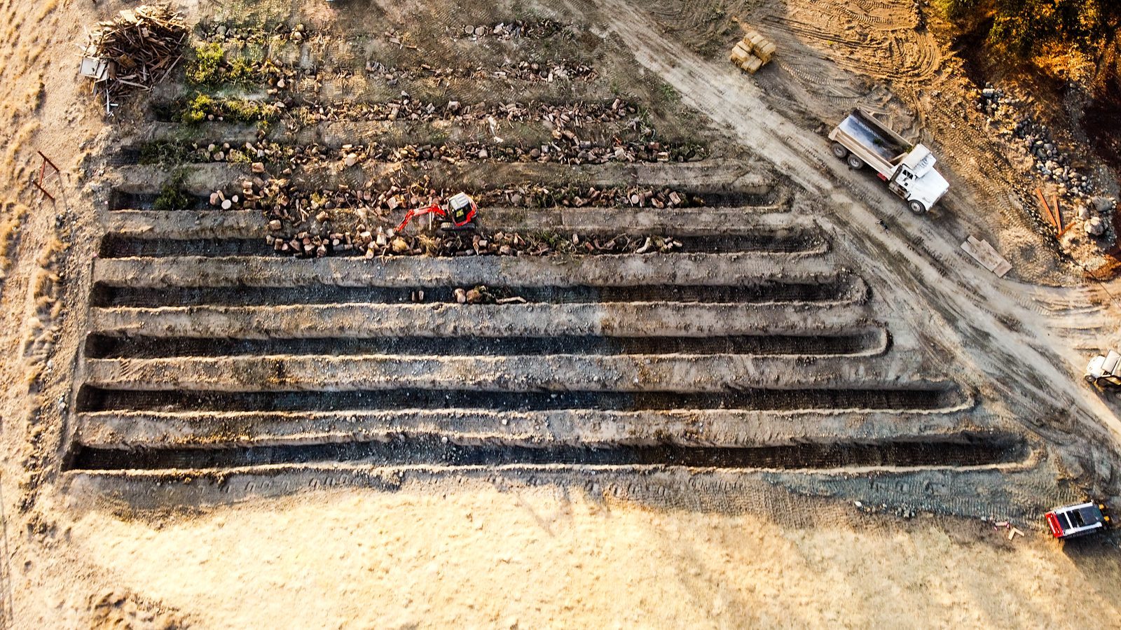 Straight-down aerial view of the parallel trenches filled end to end with whole logs, branches and leaves before the soil is returned.
