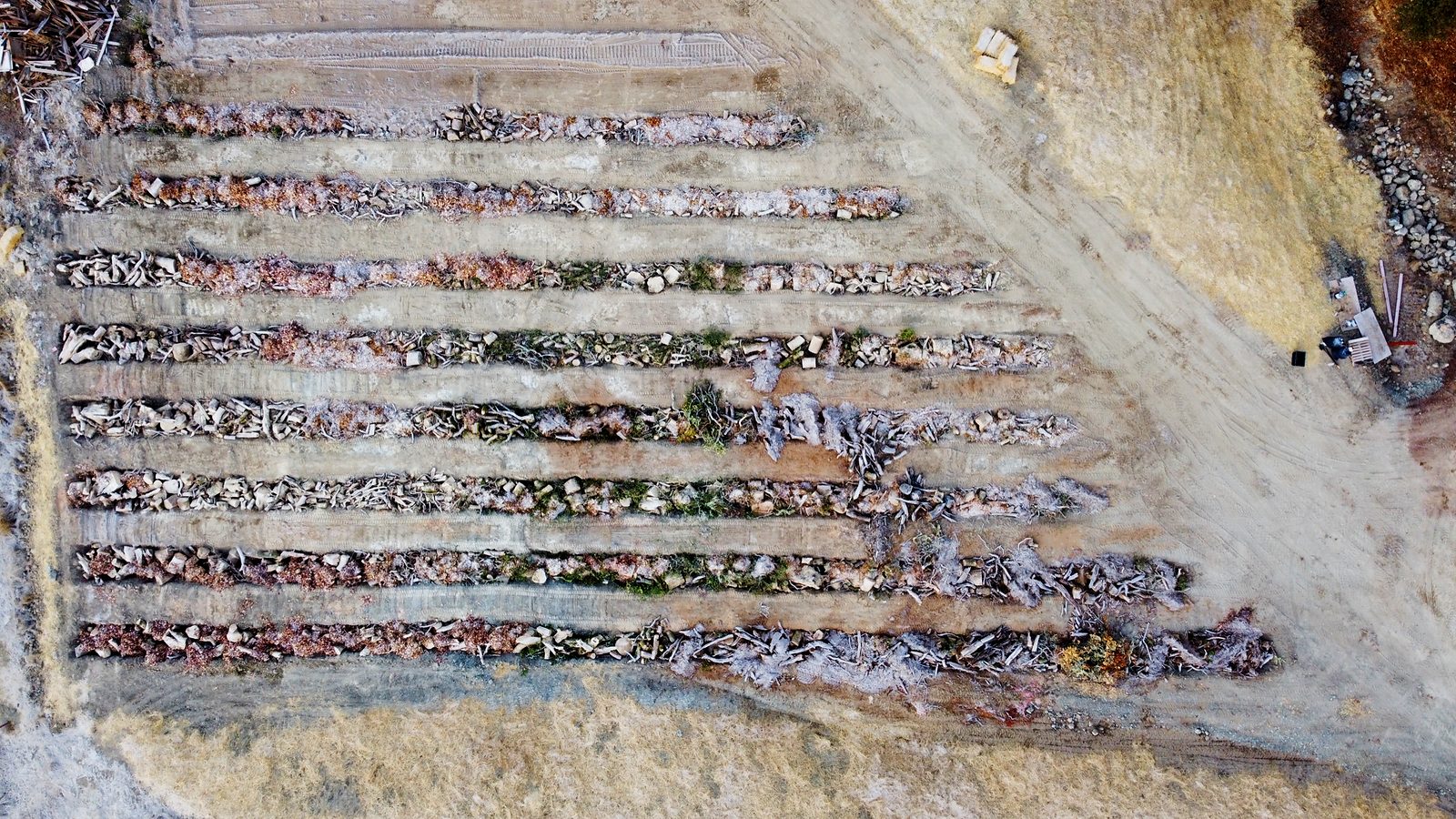 Aerial view of the hugelkultur beds under active construction, with an excavator and dump truck working among the open trenches.