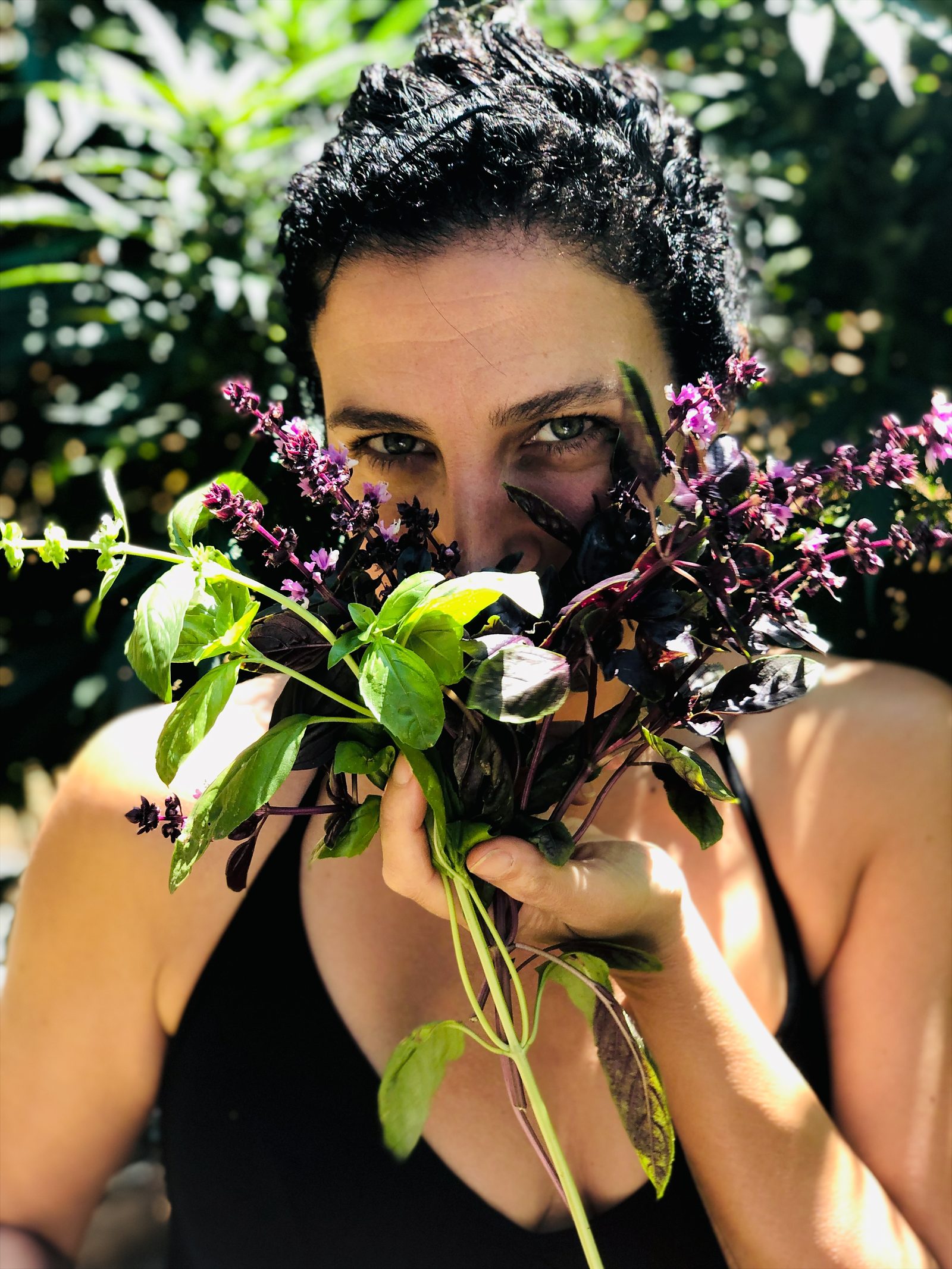 A woman looking through a freshly gathered bouquet of green and purple flowering herbs in the garden.